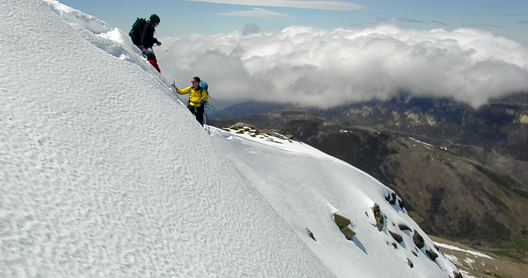 Dos montañeros ascienden una ladera nevada cerca de la cumbre de El Cabezo de Serranillos, en invierno.